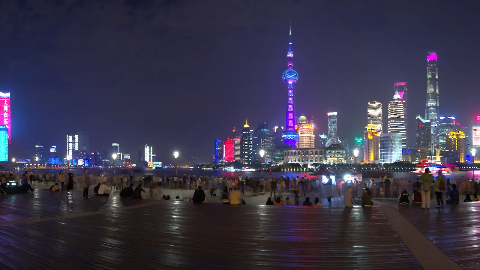 The Shanghai skyline at night seen across the river from the Bund. Left of the wipe the frame is straight off the sensor data — hazy, washed out and violet-cast. Right of it a Nyans grade has set the black point, corrected the balance and brought the neon back.